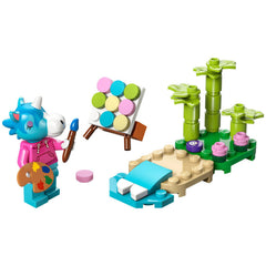 Lego Animal Crossing construction set featuring Julian, a colorful unicorn character, painting on an easel beside a beach scene with palm trees and flowers.