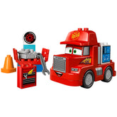 Vibrant red Mack truck from Disney and Pixar's Cars, featuring eyes and a smiling mouth, next to a brick-built tuning station with an engine and wrench.