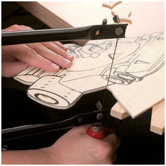 Hands using a fretsaw to cut a detailed drawing on a birch plywood plate.