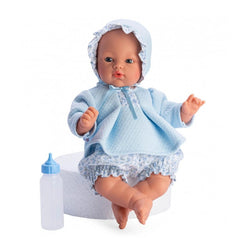 Soft-bodied doll with blue eyes and a bonnet, wearing a blue and flowered outfit, sitting next to a toy bottle.