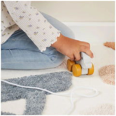 A child gently holds a gray and yellow pull-along elephant toy, sitting on a soft, textured carpet with pastel shapes.