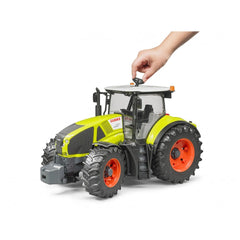 Hand steering a detailed Claas Axion 950 toy tractor with bright green body and large orange wheels.