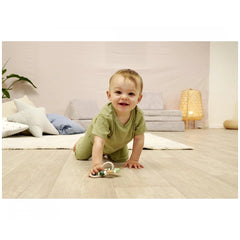 Eichhorn Baby HiPP Grapper with Ring is featured with a smiling baby on a light wooden floor in a softly colored room.