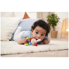 Eichhorn baby wooden teething ring rabbit beside a child on a soft surface, with a stuffed toy and green plant in the backgro