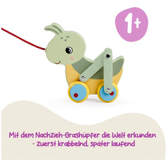 Colorful pulling grasshopper toy frog with a smiling face and red string on a yellow surface against a plain white background