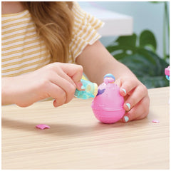 Hatchimals Alive toy with a pink body and blue head is being playfully held by a child at a light wooden table.