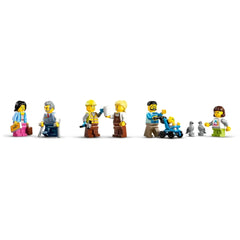 Six LEGO mini-figures at a train station scene: a ticket seller with a sign, an elderly man with a cane, a construction worker holding tools, a barista serving coffee, a parent pushing a stroller with a child, and a woman with two pigeons nearby.