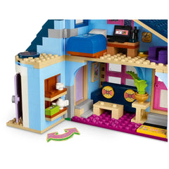 Colorful interior of a LEGO® Friends house featuring a blue bed, a desk with a computer, and a cozy seating area with a plant.
