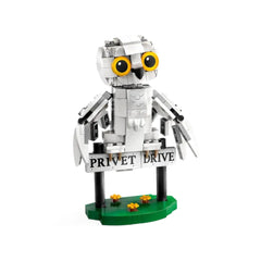 Posable white snowy owl figure, Hedwig, perched on a black sign reading "Privet Drive," set on a green base with small yellow flowers.