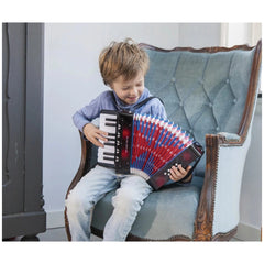 Black accordion with music book held by a young boy in a blue shirt and jeans, sitting on a blue upholstered chair.