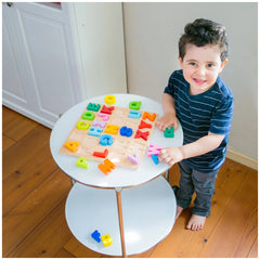 New Classic Toys Alphabet Puzzle with colorful letters and numbers, as a young child holds a wooden tray on a white table.