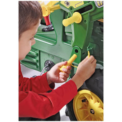 A child in a red shirt sits on the floor, focused on a green and yellow toy tractor with a yellow tool in hand.