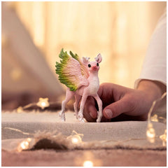 Magical Fawn figurine with pinkish-white skin and green wings held by a hand on a light brown surface.