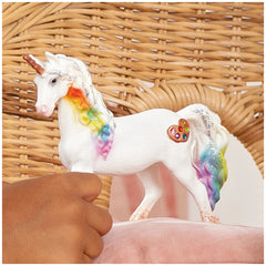 Rainbow Love Unicorn Mare figurine with multicolored mane, white body, and heart decoration on a textured brown basket.
