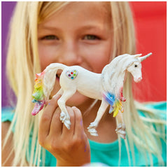 Rainbow Love Unicorn Stallion figurine with glossy white body and colorful mane, held by a girl in a light blue top.