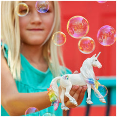 Rainbow Love Unicorn Stallion toy is held by a girl in a light blue top against a solid red background with colorful bubbles.