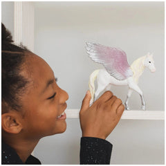 Schleich Sunrise Pegasus toy figure with a young girl in a black glittery top and a white wall with horse artwork.