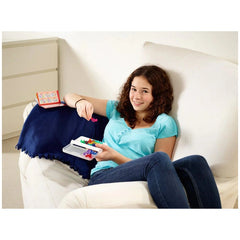 A young girl in a blue outfit smiles while holding a small, colorful object on a light-colored couch with a blue throw blanke