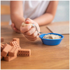 Teifoc big timber-framed house set displayed with a child's hands holding a spoon and clay-like objects on a wooden surface.