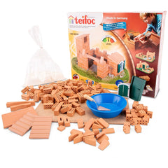 Teifoc castle-house construction set with orange bricks, a blue bowl, and sand scattered on a light surface.