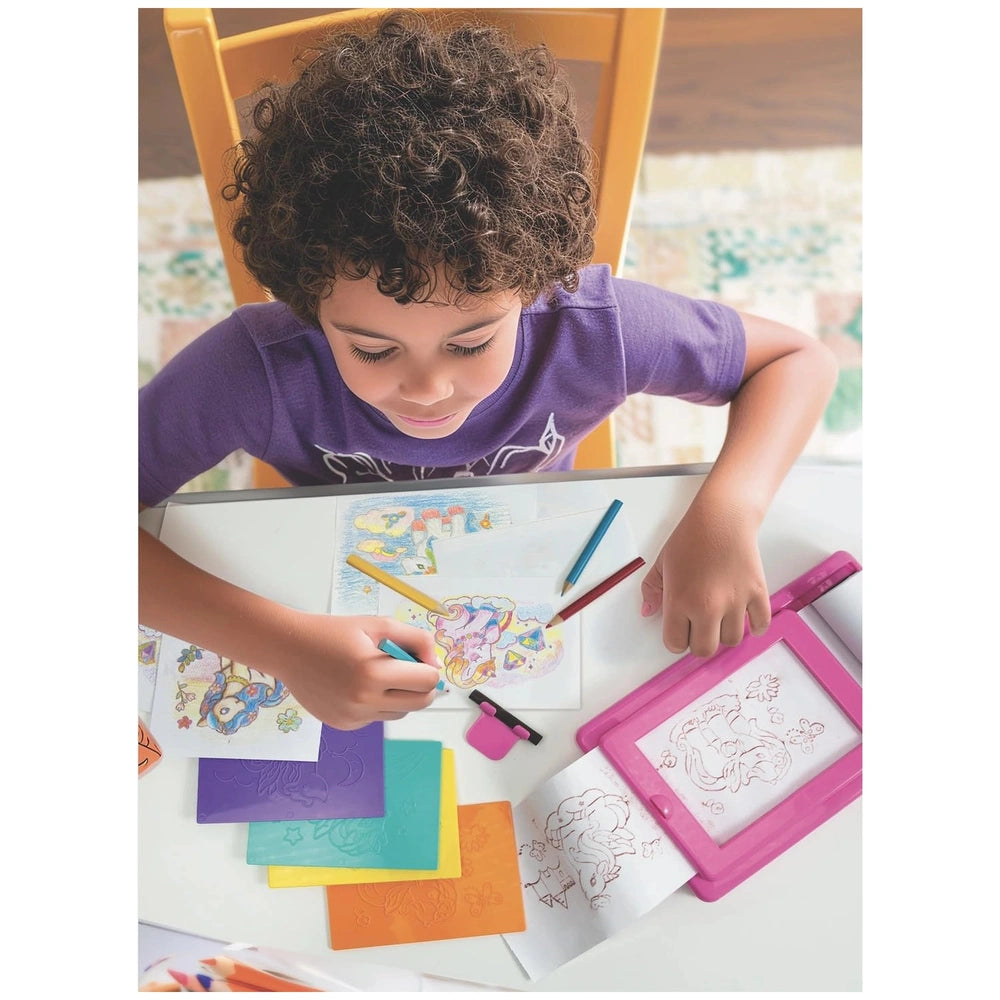 child, surrounded by colorful markers and erasers on a white table while creating art with the 4M KidzMaker Unicorn Rub Art S