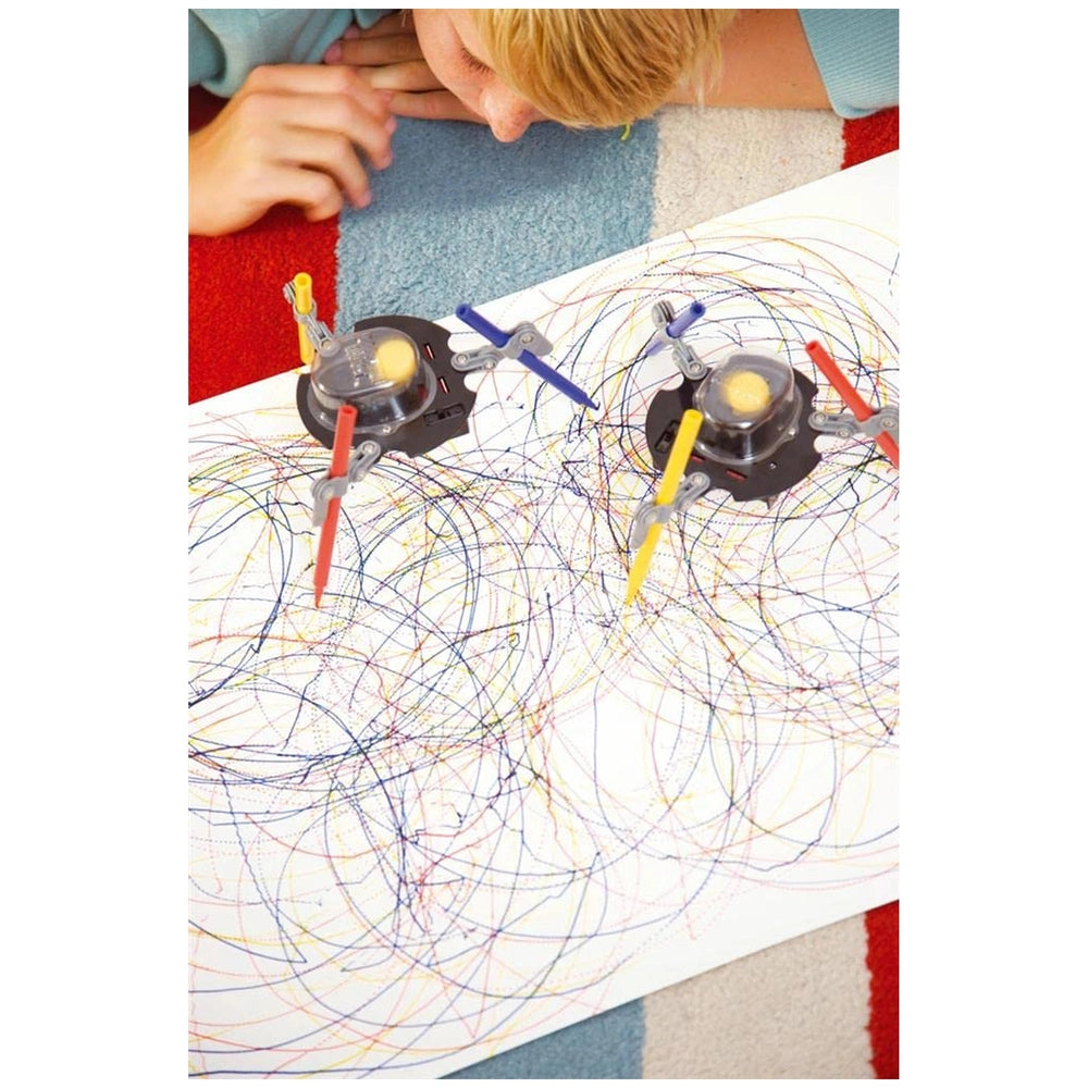KidzRobotix Doodling Robot with yellow centers surrounded by blue and red lines on a patterned rug with a person's hand.