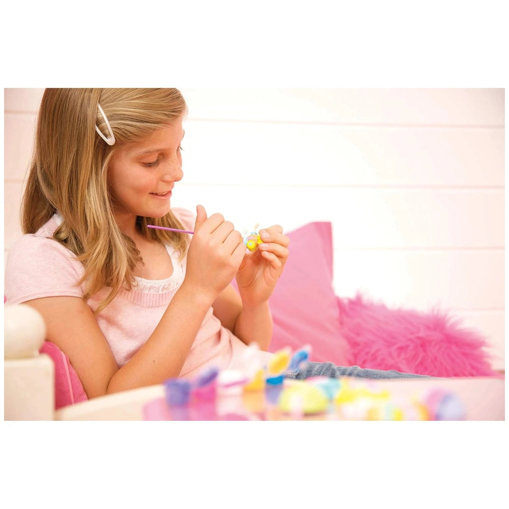 Blonde girl in pink shirt and headband holds a pink toothbrush while sitting on a pink chair near a white wall.