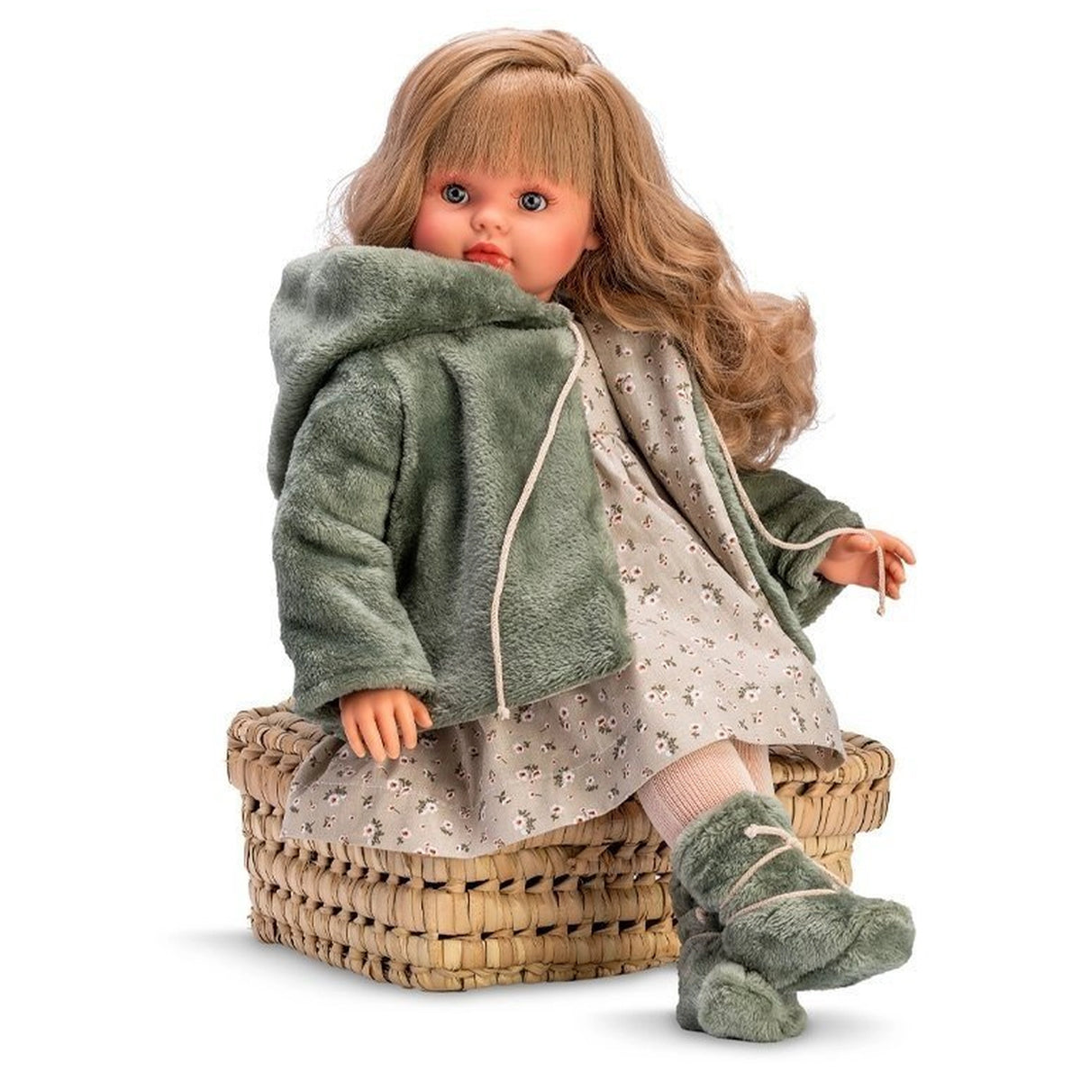 ASI Pepa doll in green coat and floral dress, seated on woven basket, with soft boots and lifelike features.