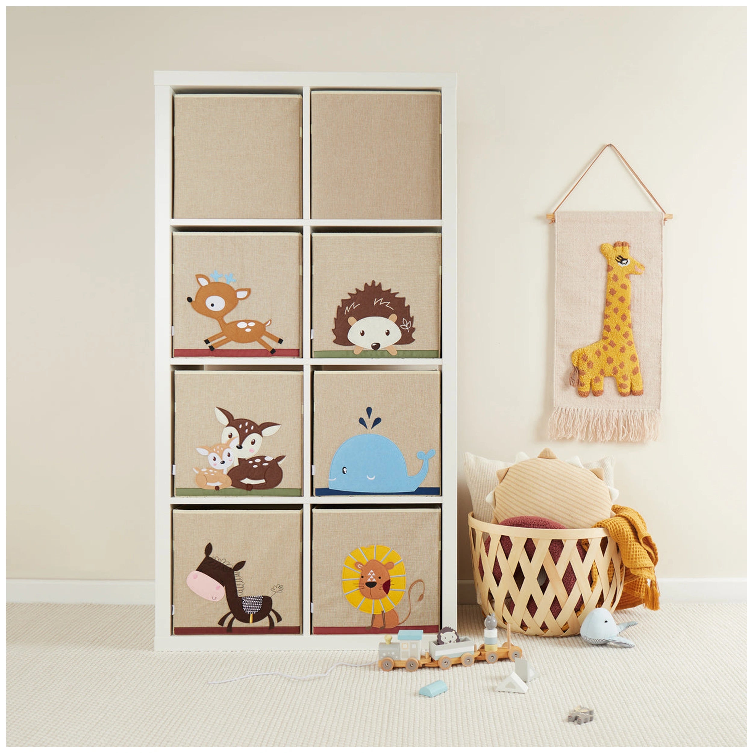 Whale, deer, hedgehog, and lion designs on beige storage boxes in a white shelving unit, with a giraffe wall hanging nearby.