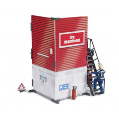 Red toy fire station with "fire department" sign, grey stairs, and firefighter figure climbing. Includes a parking sign and extinguisher.