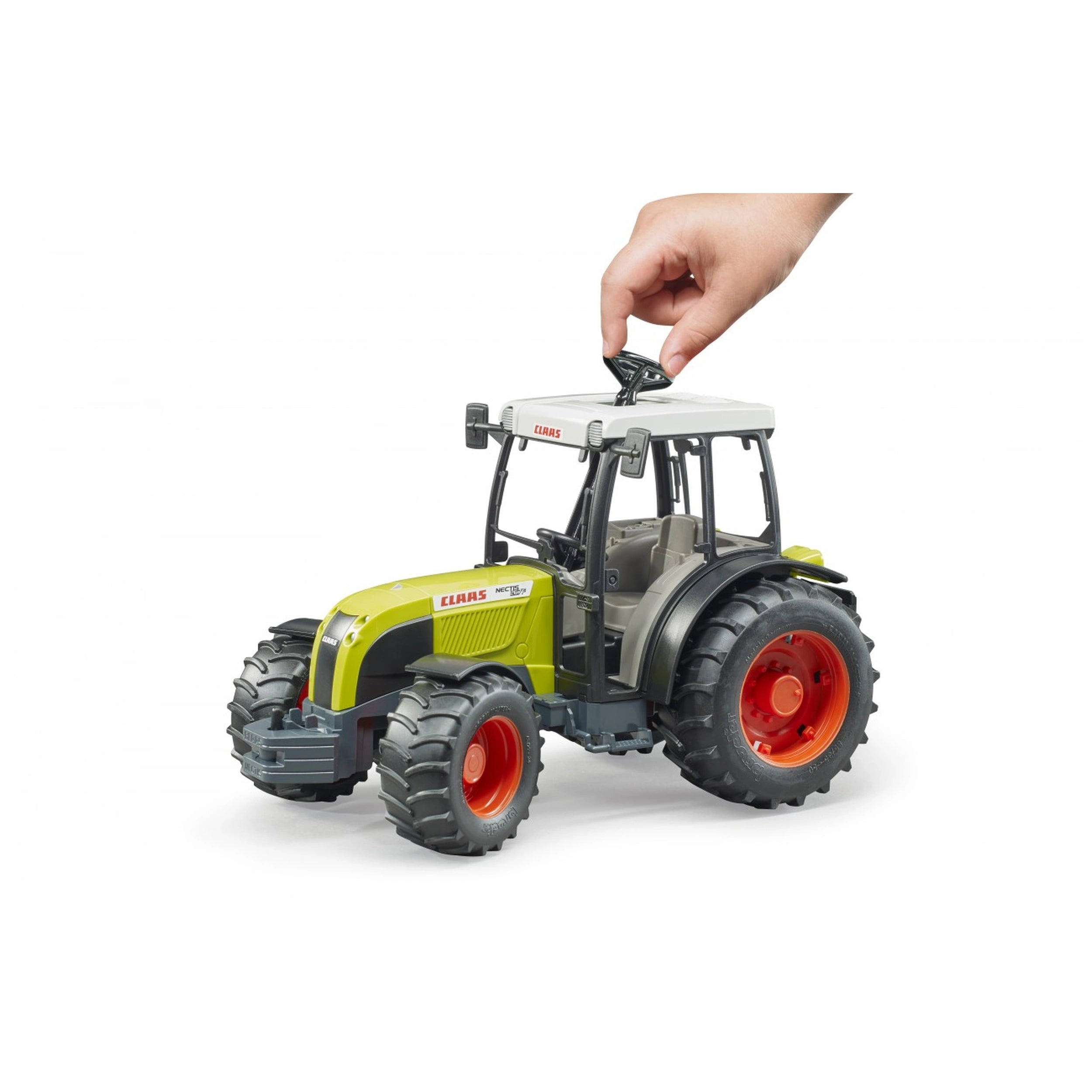 Hand adjusting the roof of a green and white Bruder Claas Nectis 267 F toy tractor with red wheels.