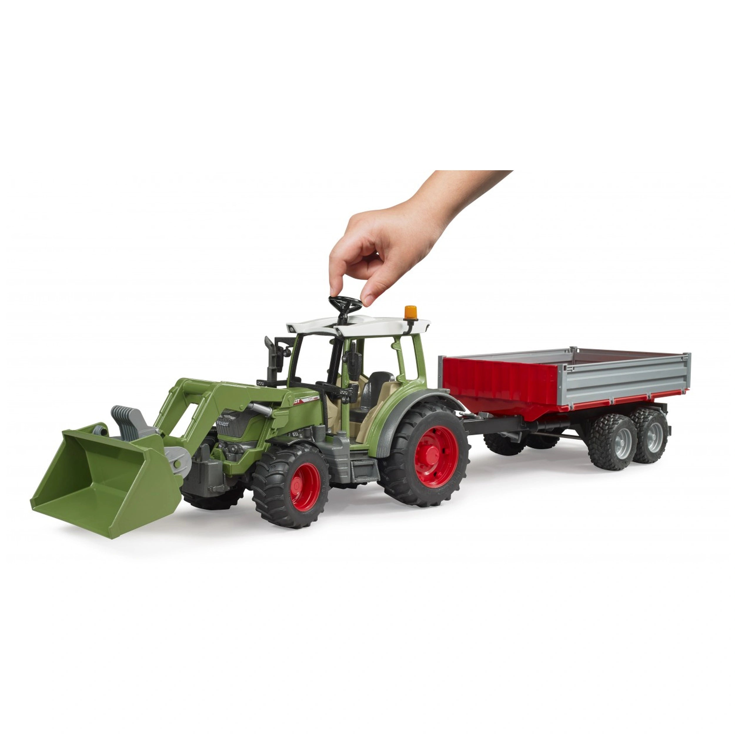 Green toy tractor with a frontloader and red tipping trailer, operated by a child's hand, on a white background.