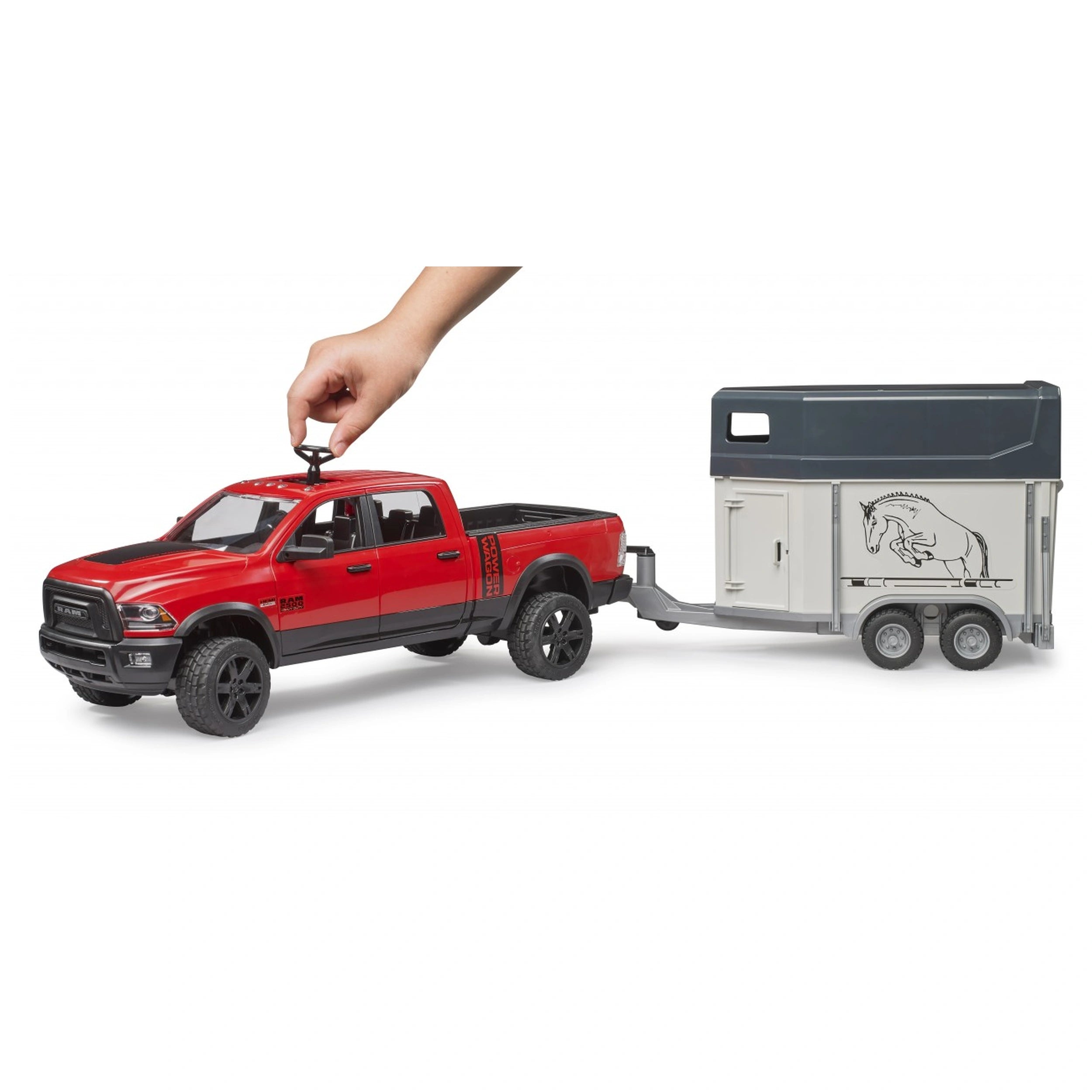 Red toy RAM 2500 truck hitched to a horse trailer, with a hand interacting, showcasing realistic details.