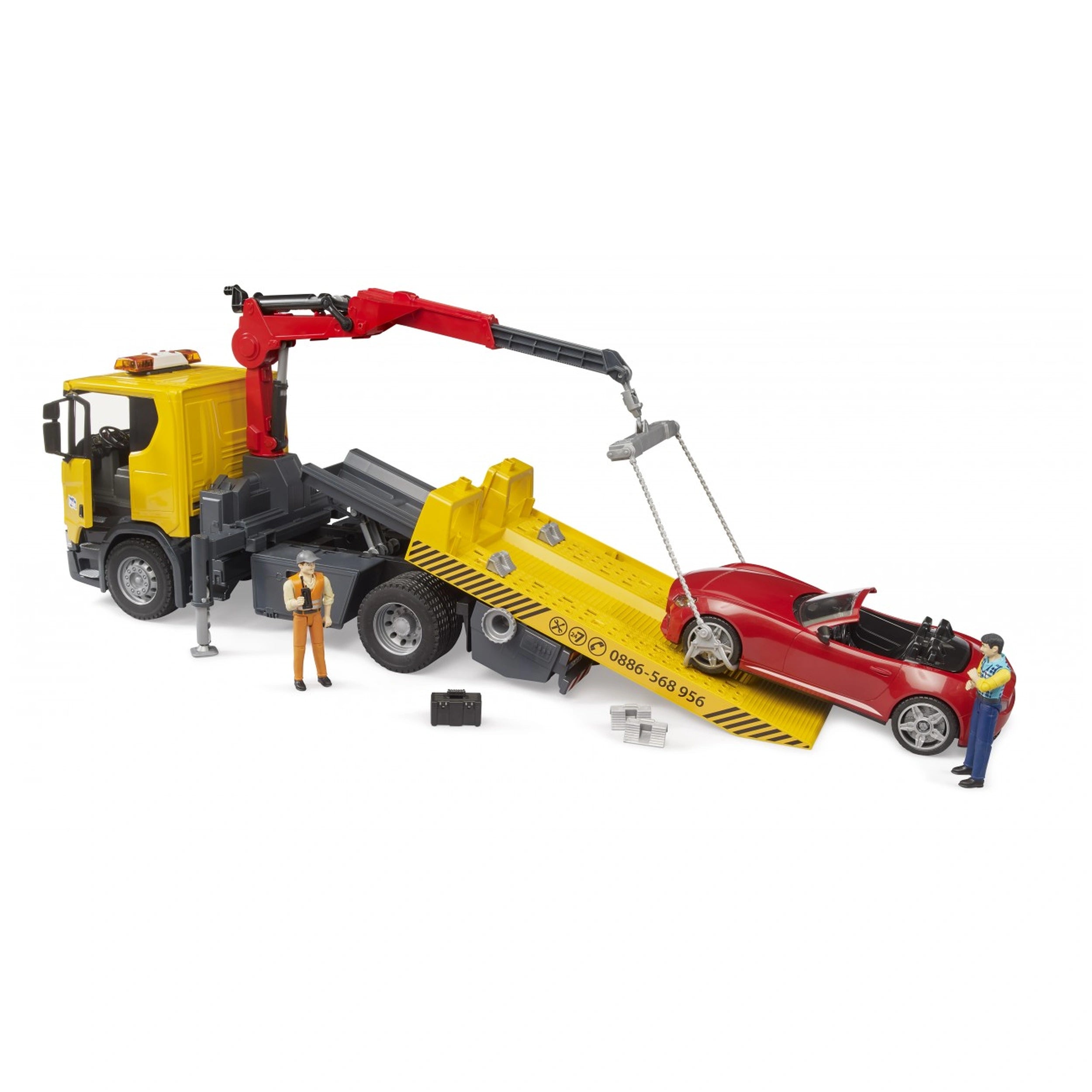 Yellow Bruder Scania tow truck with crane lifting red roadster; two figures in work attire stand nearby.