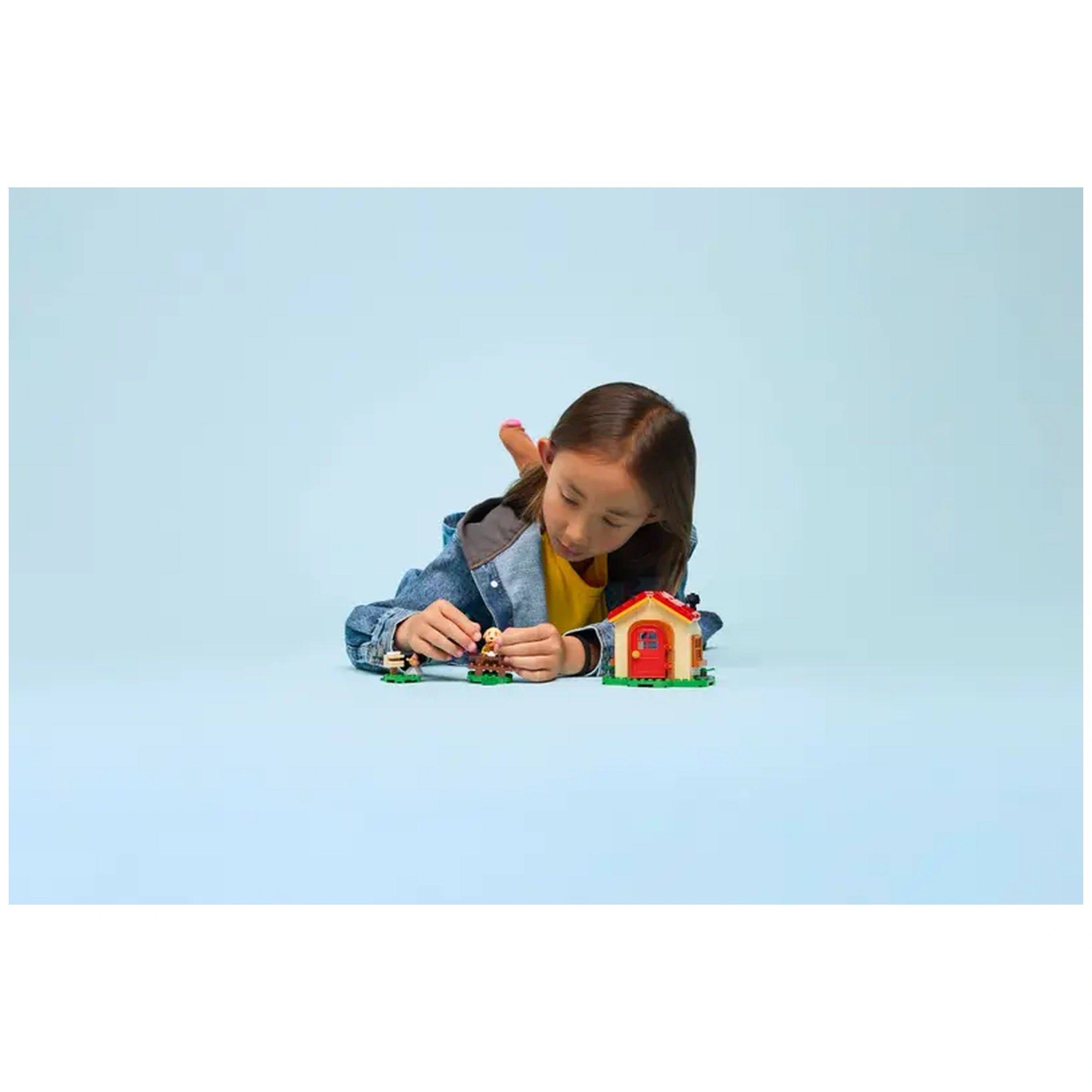 A child focuses on assembling the LEGO Goldie's Cozy House set, featuring a colorful house and minifigure, against a soft blue background.