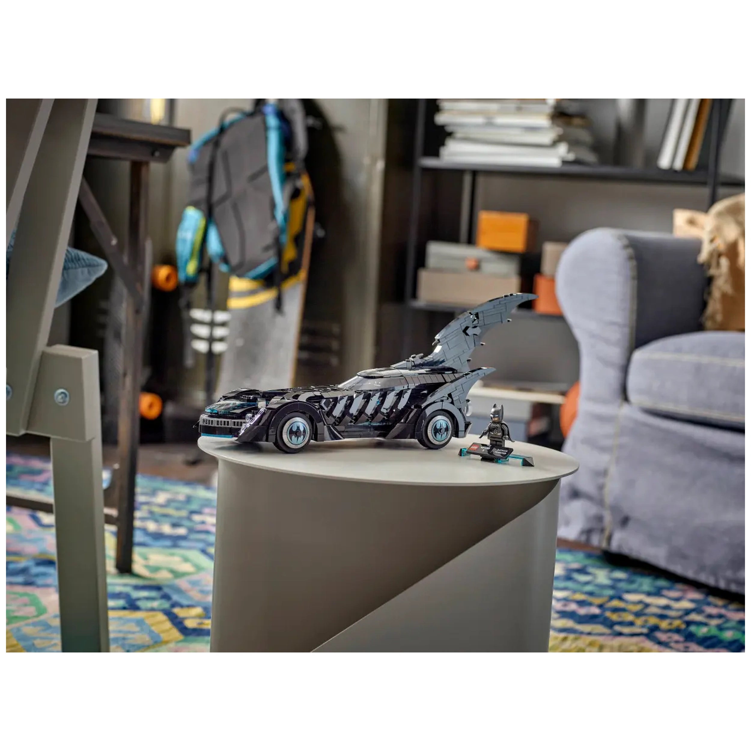 LEGO Batman Forever Batmobile model displayed on a round gray table, with a Batman minifigure beside it, set in a cozy room.