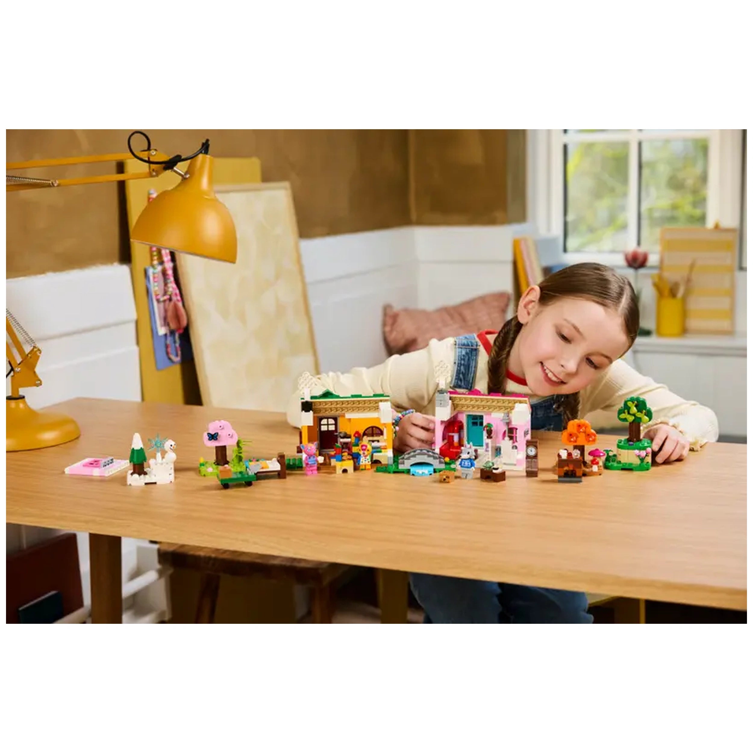 A smiling girl intently plays with the LEGO Creative Houses: Seasons of Fun set, showcasing two colorful houses and various accessories on a wooden table. A modern lamp illuminates her creative setup in a cozy room.