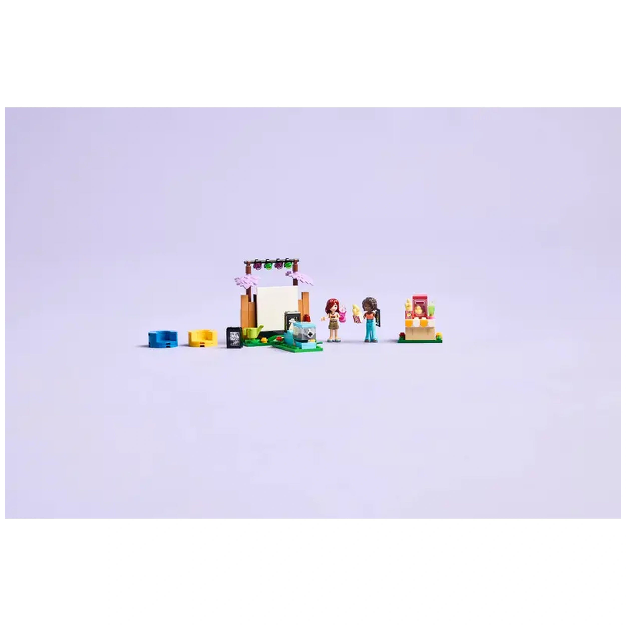 Two LEGO Friends minidolls, Paisley and Aliya, stand beside a mini projector in a garden setting, with colorful accessories for a movie night.