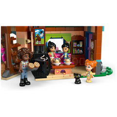 Three LEGO characters engage in playful activity inside a cozy pony ranch setting. One character holds a tray of cookies, while two others chat near a kitchen area decorated with colorful accessories. A playful black cat sits nearby, adding to the inviting atmosphere.