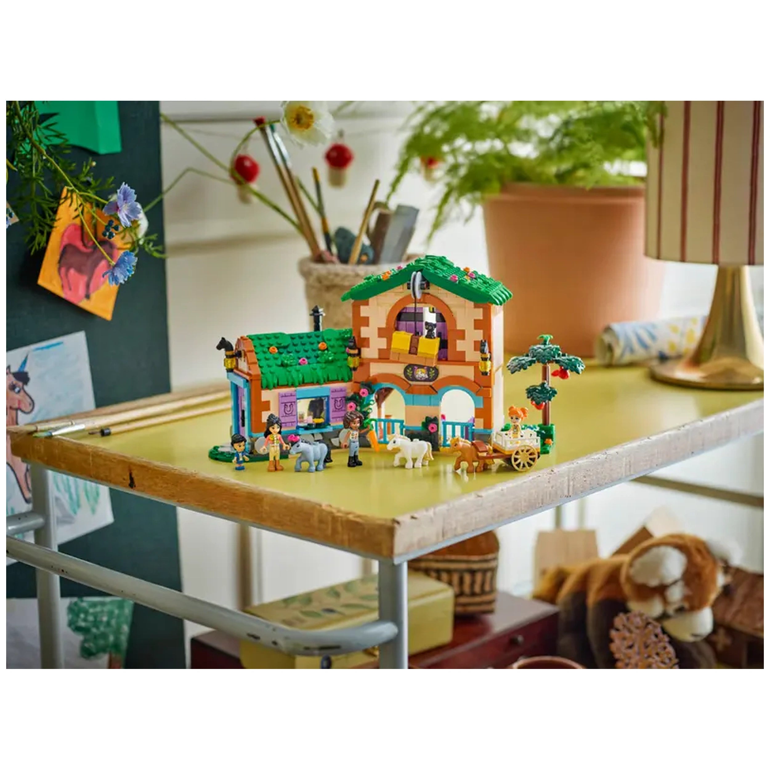 Colorful LEGO Friends Pony Ranch set on a wooden table, featuring a stable with characters, three ponies, and a cart.