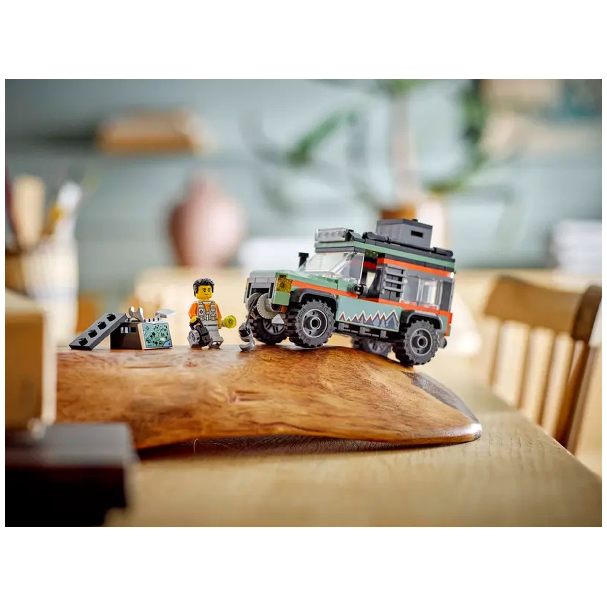 LEGO City Off-Road Mountain Truck set on a wooden table, accompanied by a minifigure holding a yellow tool, with a backdrop of a cozy room.
