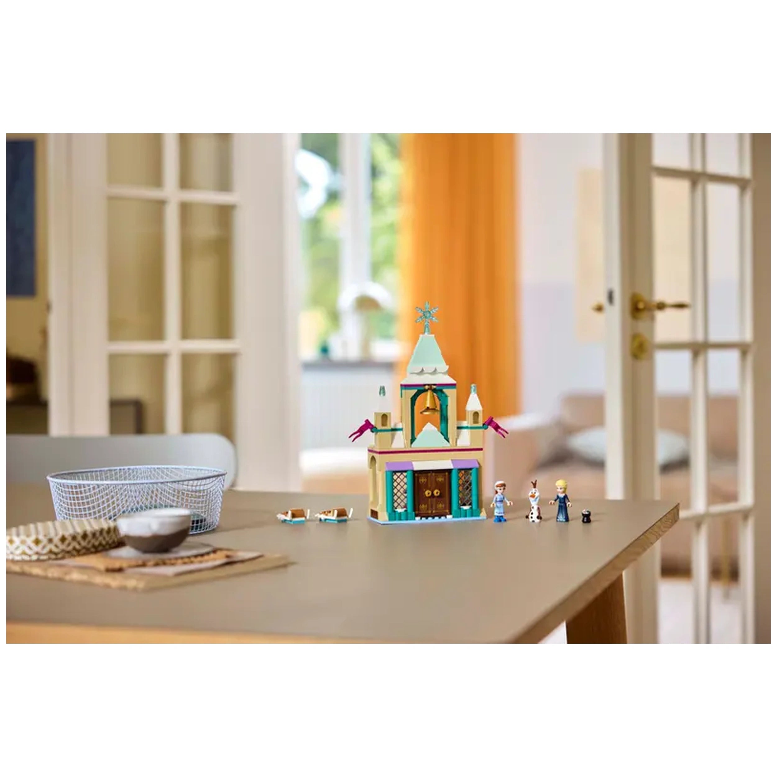 Colorful LEGO Disney Frozen Arendelle Castle set on a wooden table, featuring Elsa, Anna, and Olaf figures, with a cozy room backdrop.