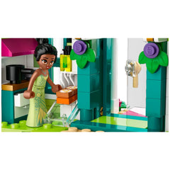 A Lego figure of Tiana in a green dress, smiling as she reaches for a box in a colorful kitchen setting from the Disney Princess Market Adventure set.