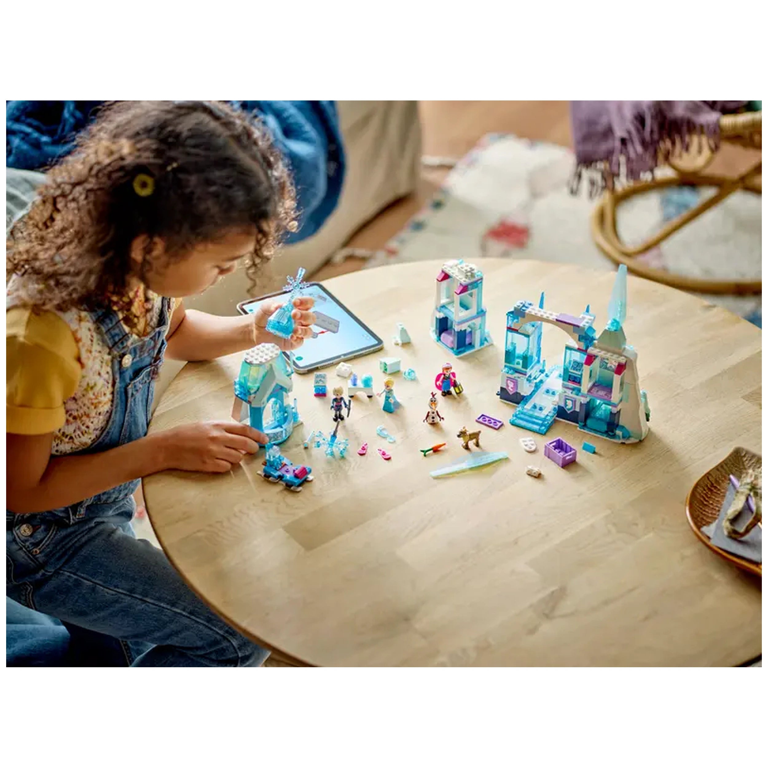 A child plays with Lego Disney Frozen Elsa's Ice Palace construction set on a wooden table, surrounded by colorful building pieces and figures.