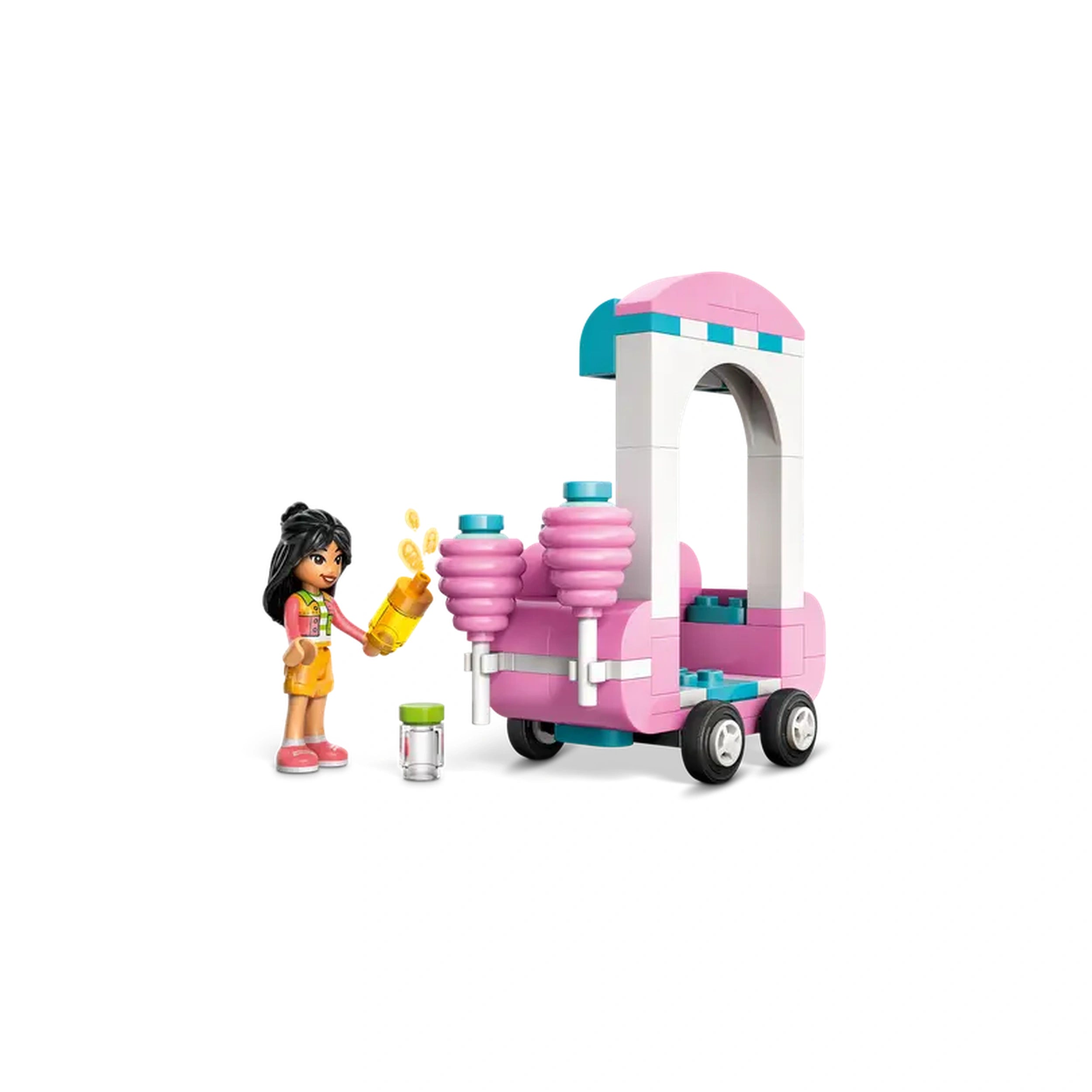 A LEGO® Friends minidoll stands beside a pink cotton candy stand with two fluffy treats. She holds a yellow bottle, preparing to serve. A small transparent container sits nearby. The scene is playful and colorful, perfect for imaginative adventures.
