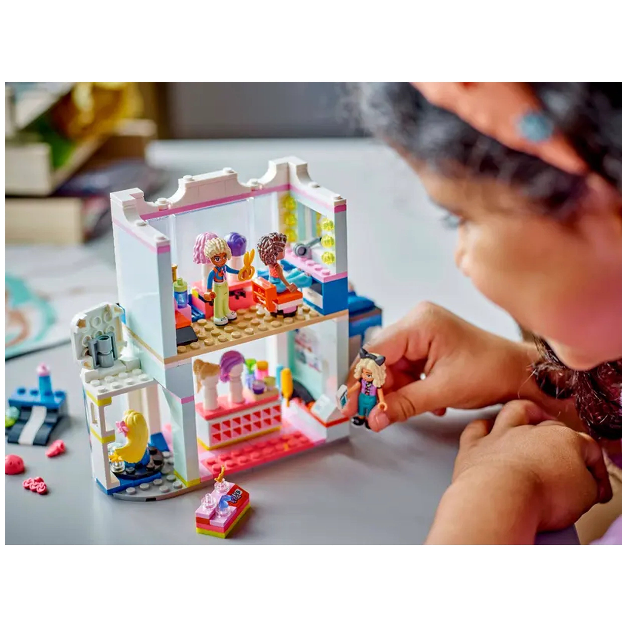 A child interacts with the LEGO® Friends Hair Salon and Accessories Store set, featuring intricate details like styling chairs and vibrant hair accessories. Three mini-dolls are positioned in the two-story salon, enhancing imaginative play.