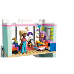 LEGO Friends Hair Salon featuring three mini-dolls at a two-story salon setup. One doll holds a hairdryer, while another styles a mannequin's hair. Bright colors, a styling chair, and decorative accessories create a playful atmosphere.