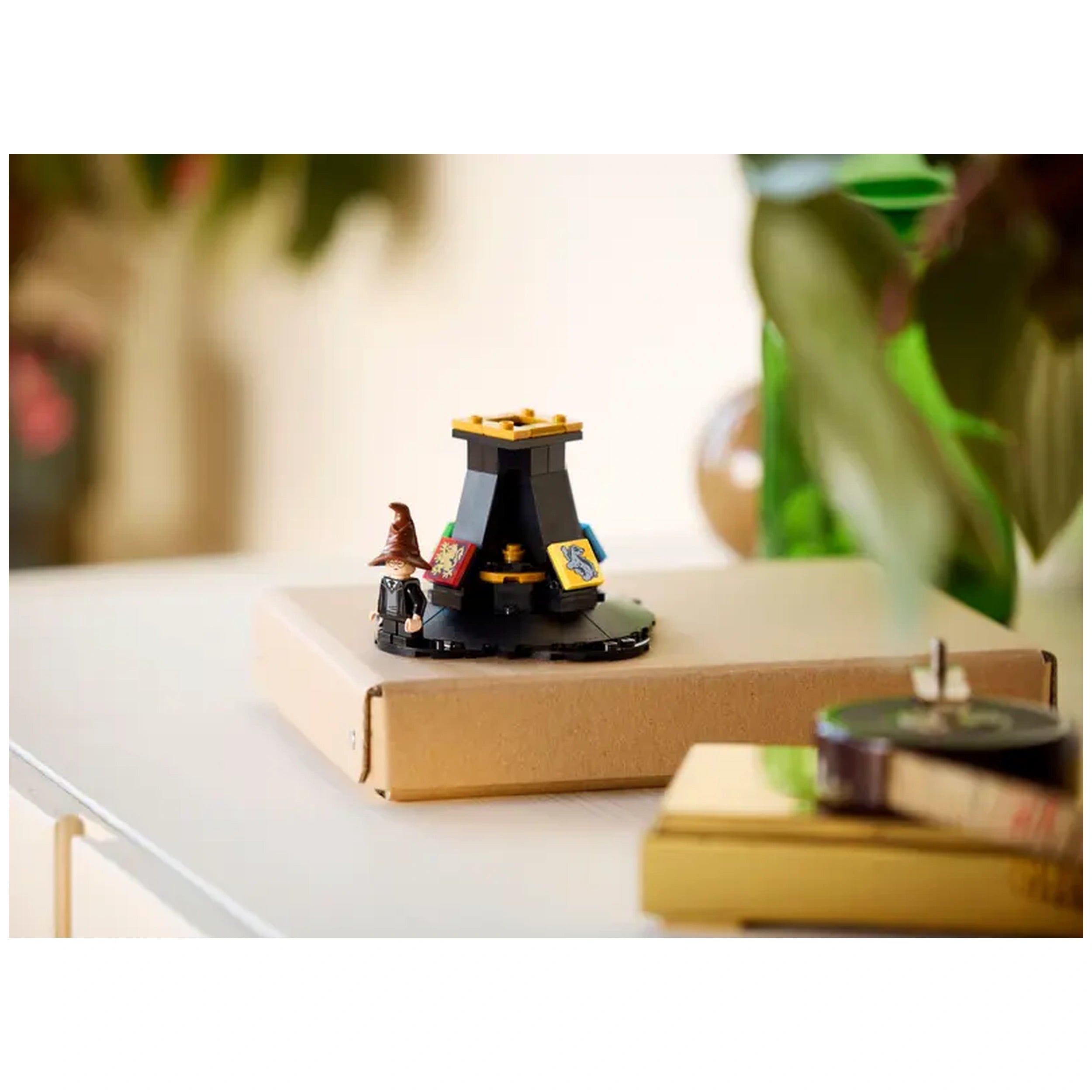 Lego Harry Potter Talking Sorting Hat on a cardboard box, featuring iconic house emblems and a detailed hat figurine, in a cozy setting.