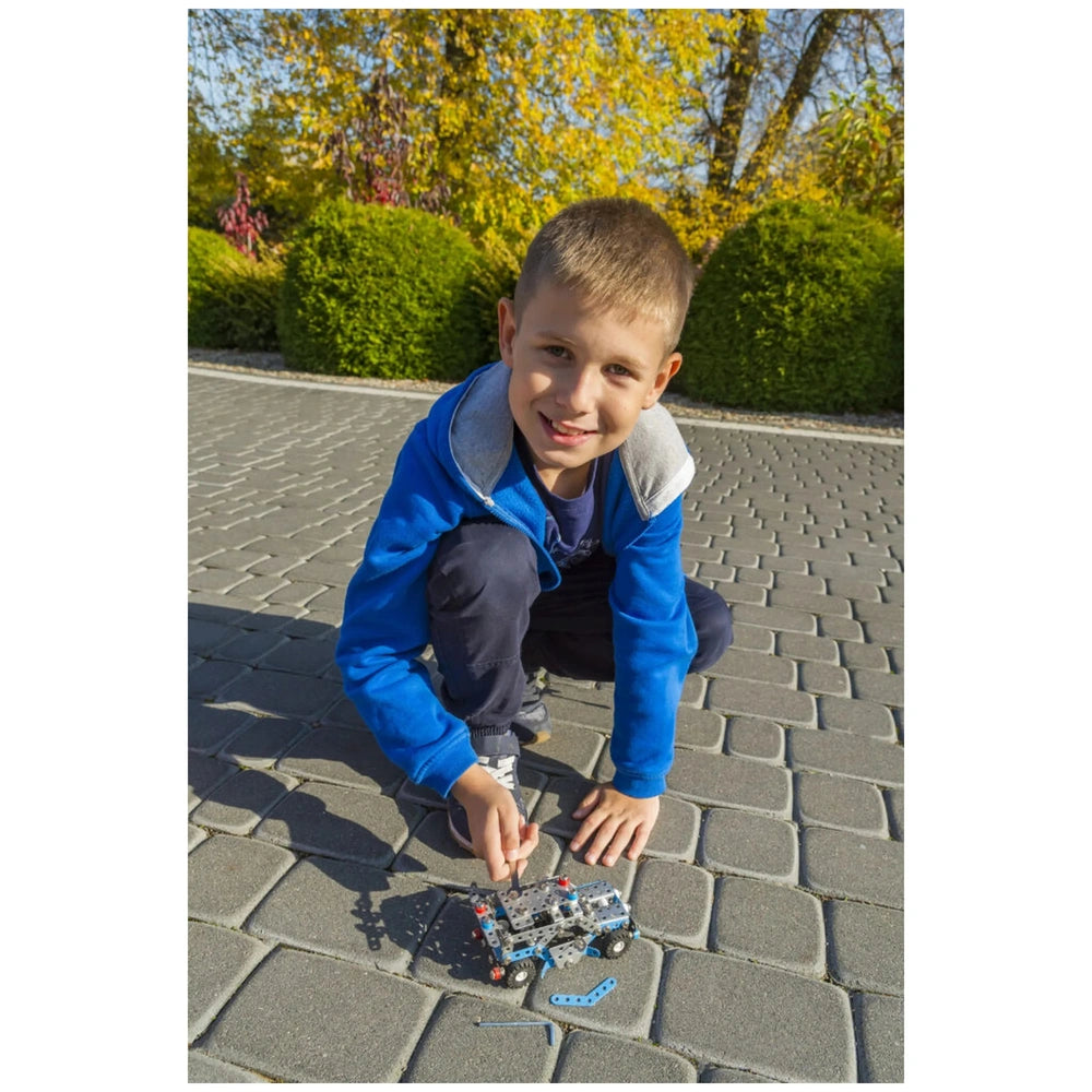Young boy assembling Alexander Constructor Police Car set on a sunny day, kneeling on cobblestone pavement.