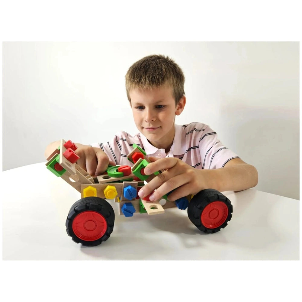 Young boy assembling a colorful buggy with Alexander Maly Constructor Junior set, focusing intently on the wooden and plastic pieces.